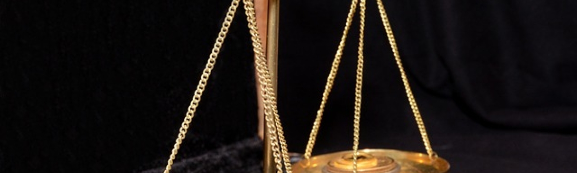 Abbildung einer altertümlichen, goldenen Waage. Sie schwebt knapp über einem Holztischchen mit schwarz bezogener Samtoberfläche. In den Waagschalen liegen einige Goldmünzen. 