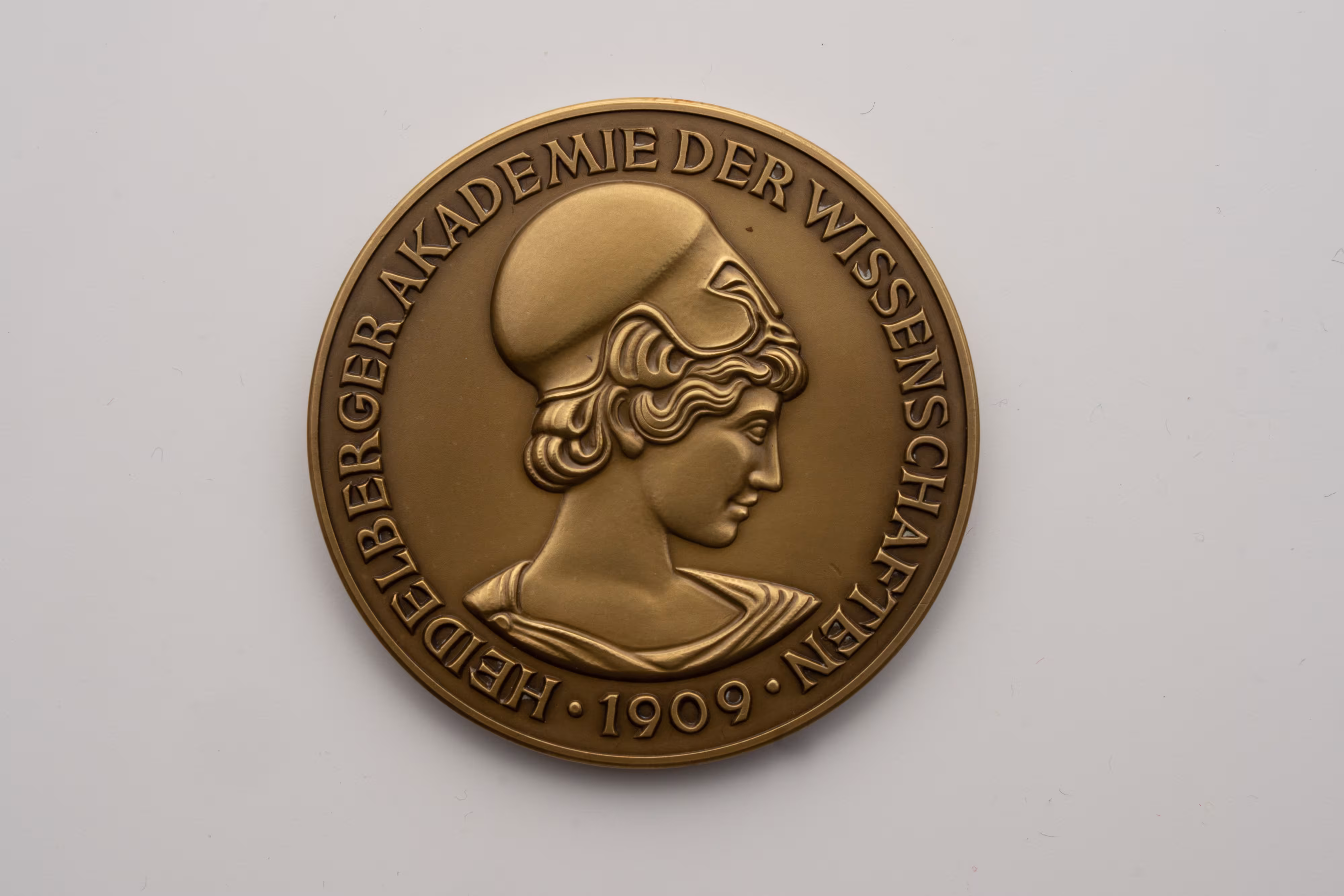 Die Bronzemedaille zeigt den Kopf der Athene als griechischer Göttin der Wissenschaft. Am Rand der Medaille verläuft der Schriftzug Heidelberger Akademie der Wissenschaften 1909.   
