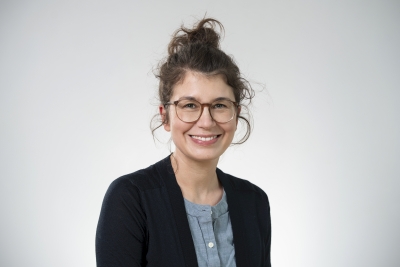 Dreiviertelporträt von Stefanie Gänger, die den Betrachter anlächelt. Sie trägt die braunen Haare hochgebunden und hat eine Brille.