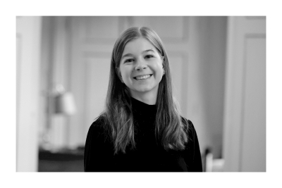 Porträtfoto von Lea Hauß. Sie wendet sich dem Betrachter lächelnd zu. Ihre Haare sind dunkelblond und fallen offen bis zur Brust.