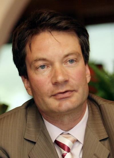 Portrait von Volker Wulfmeyer in Nahaufnahme. Er schaut leicht am Betrachter vorbei und hat den Mund leicht geöffnet. Er trägt ein braunes Jackett, darunter ein weißes Hemd und eine gestreifte Krawatte.