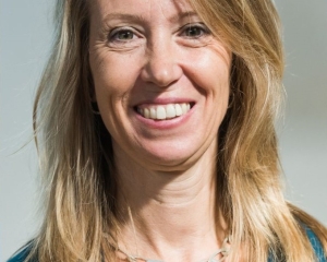 Portrait in halbnaher Aufnahme von Christiane Werner. Sie trägt die Haare offen, ein türkises Shirt und einen türkisen Blazer darüber. Dazu trägt sie eine silberne Halskette mit groben Maschen. Sie lächelt frontal in die Kamera.