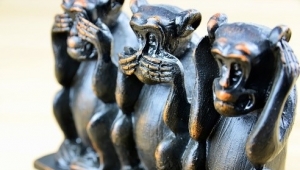 Drei aus Holz geschnitzte, schwarz bemalte Affenstatuen. Der linke Affe hält sich die Augen zu, der in der Mitte den Mund und der rechts die Ohren.