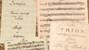 Zwei Notenblätter und zwei Titelblätter der Musikstücke liegen auf einem hellbraunen Untergrund.