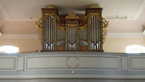 Vom Altar aus ist das Kirchenschiff mit Orgel aufgenommen. Die Orgel ist auf einer Empore angebracht. Die metallernen Flöten werden von Goldschmuck umrahmt und sind mit einer hölzernen Verkleidung eingefasst. An der Kirchendecke über den braunen Kirchenbänken ist eine Deckenmalerei zu sehen.