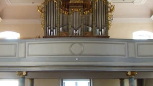 Vom Altar aus ist das Kirchenschiff mit Orgel aufgenommen. Die Orgel ist auf einer Empore angebracht. Die metallernen Flöten werden von Goldschmuck umrahmt und sind mit einer hölzernen Verkleidung eingefasst. An der Kirchendecke über den braunen Kirchenbänken ist eine Deckenmalerei zu sehen.