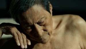 Still aus dem Dokumentarfilm "Man in Black". Zu sehen sind der auf die Hand gestützte nach unten blickende Kopf und der unbekleidete Oberkörper bis zu Brust von dem chinesischen Künstler Wang Xilin.