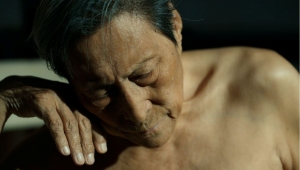 Still aus dem Dokumentarfilm "Man in Black". Zu sehen sind der auf die Hand gestützte nach unten blickende Kopf und der unbekleidete Oberkörper bis zu Brust von dem chinesischen Künstler Wang Xilin.